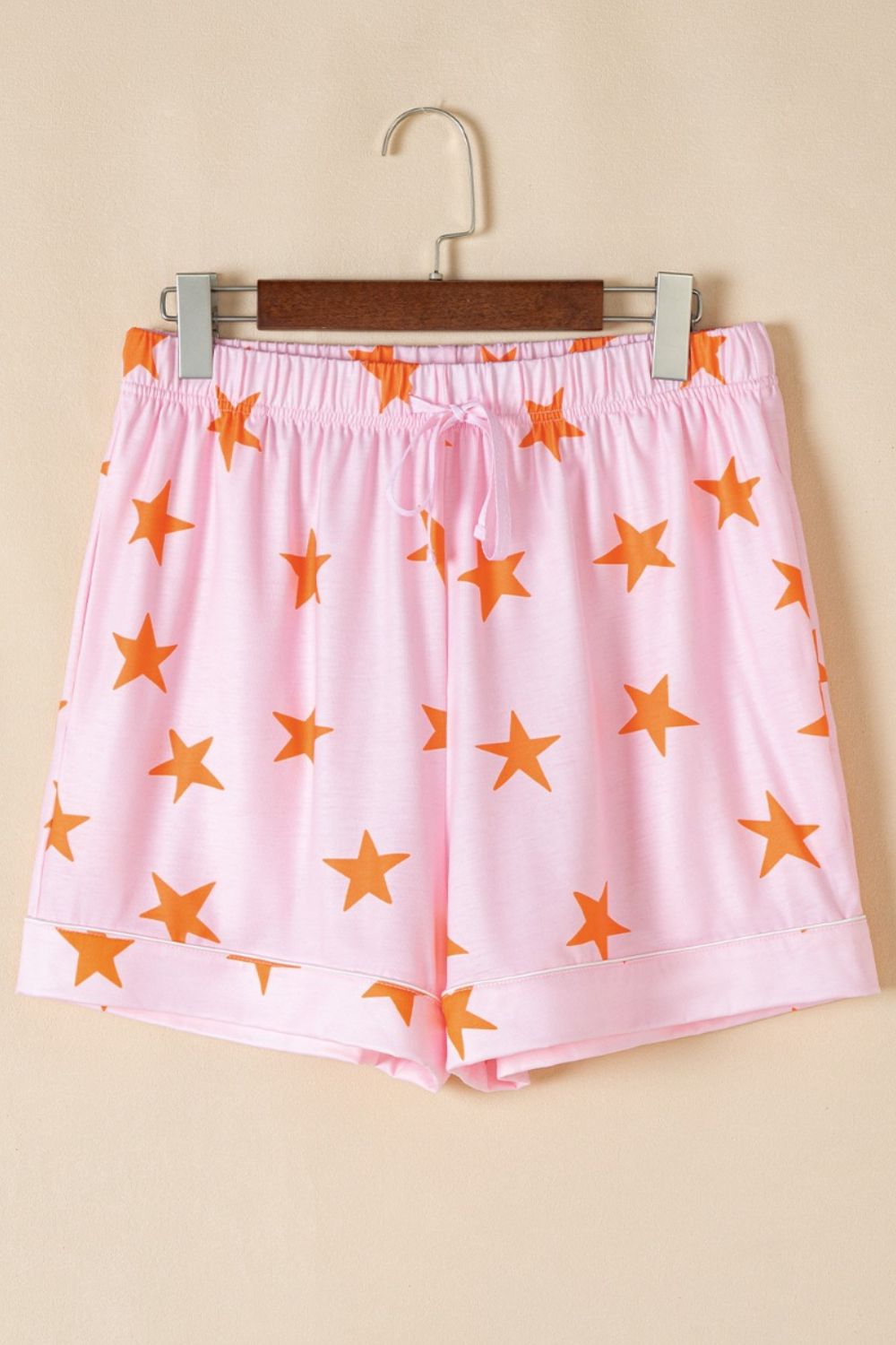 Blush pink pajama shorts with orange stars, elastic waist, and drawstring.