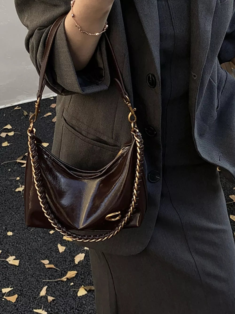 Chic crescent shoulder bag in brown patent leather with gold chain strap and detail.