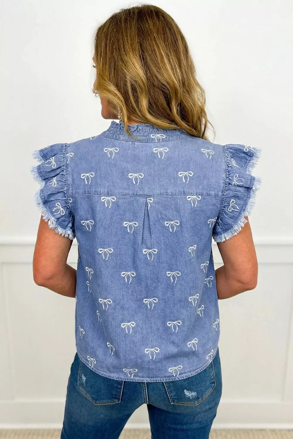 Denim blouse with ruffled sleeves, bow pattern, and frayed hem.
