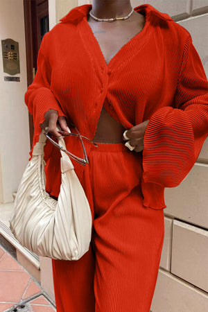 Orange-red pleated shirt and wide-leg trousers set with bell sleeves and a collared neckline.