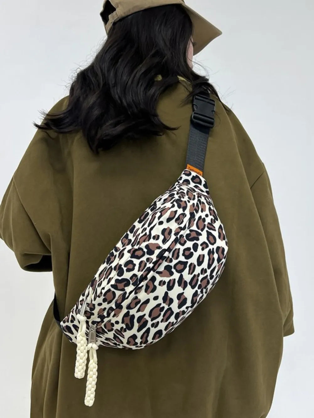 Pleated leopard print sling bag with white braided zipper pulls.
