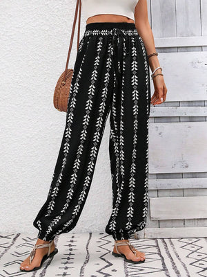 Black gathered ankle trousers with white leaf print and drawstring waist.