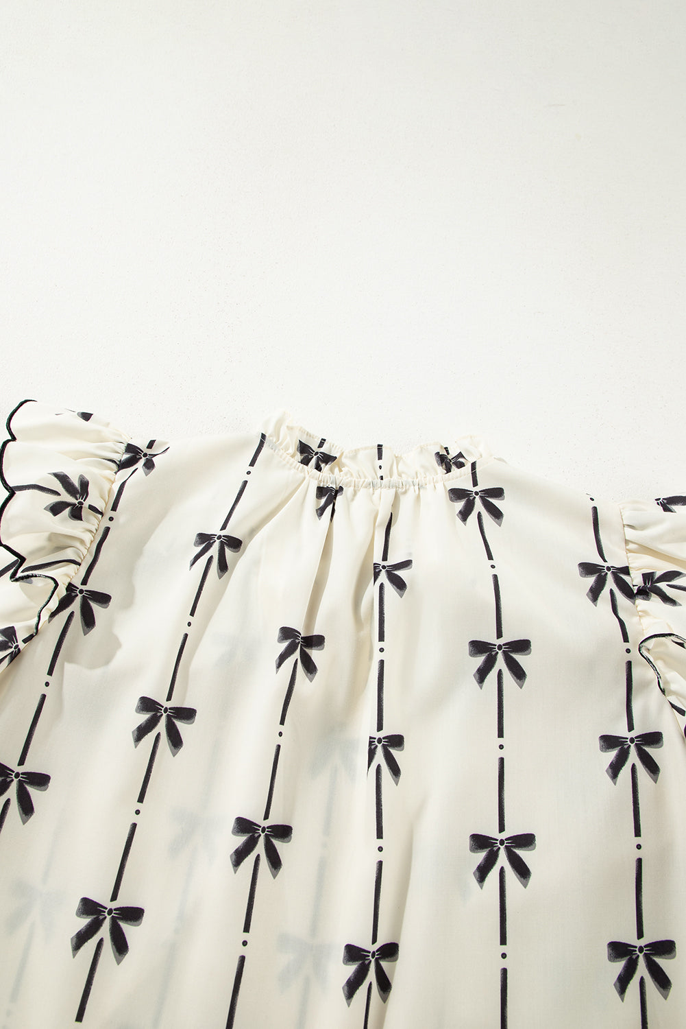 Ivory blouse with black bow print, ruffled sleeves, and a gathered neckline.