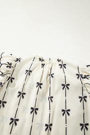 Ivory blouse with black bow print, ruffled sleeves, and a gathered neckline.