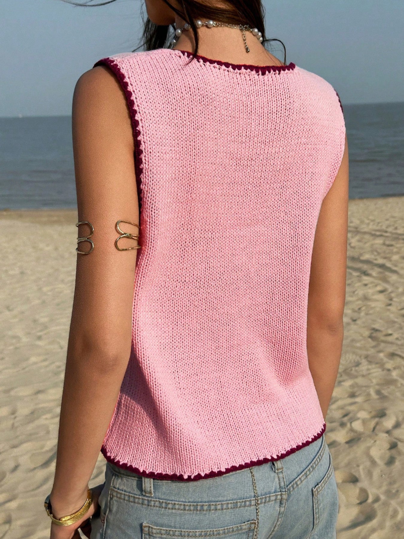 Pink knit sweater vest with contrast trim and scalloped hem.