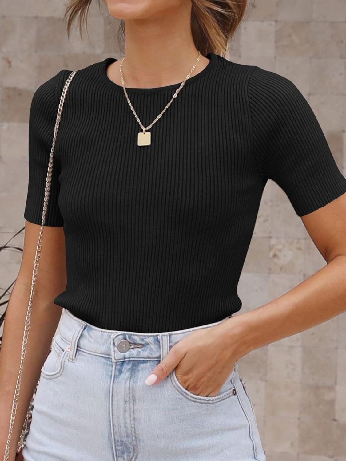 Black ribbed knit t-shirt with short sleeves and a crew neck, styled with light wash jeans.