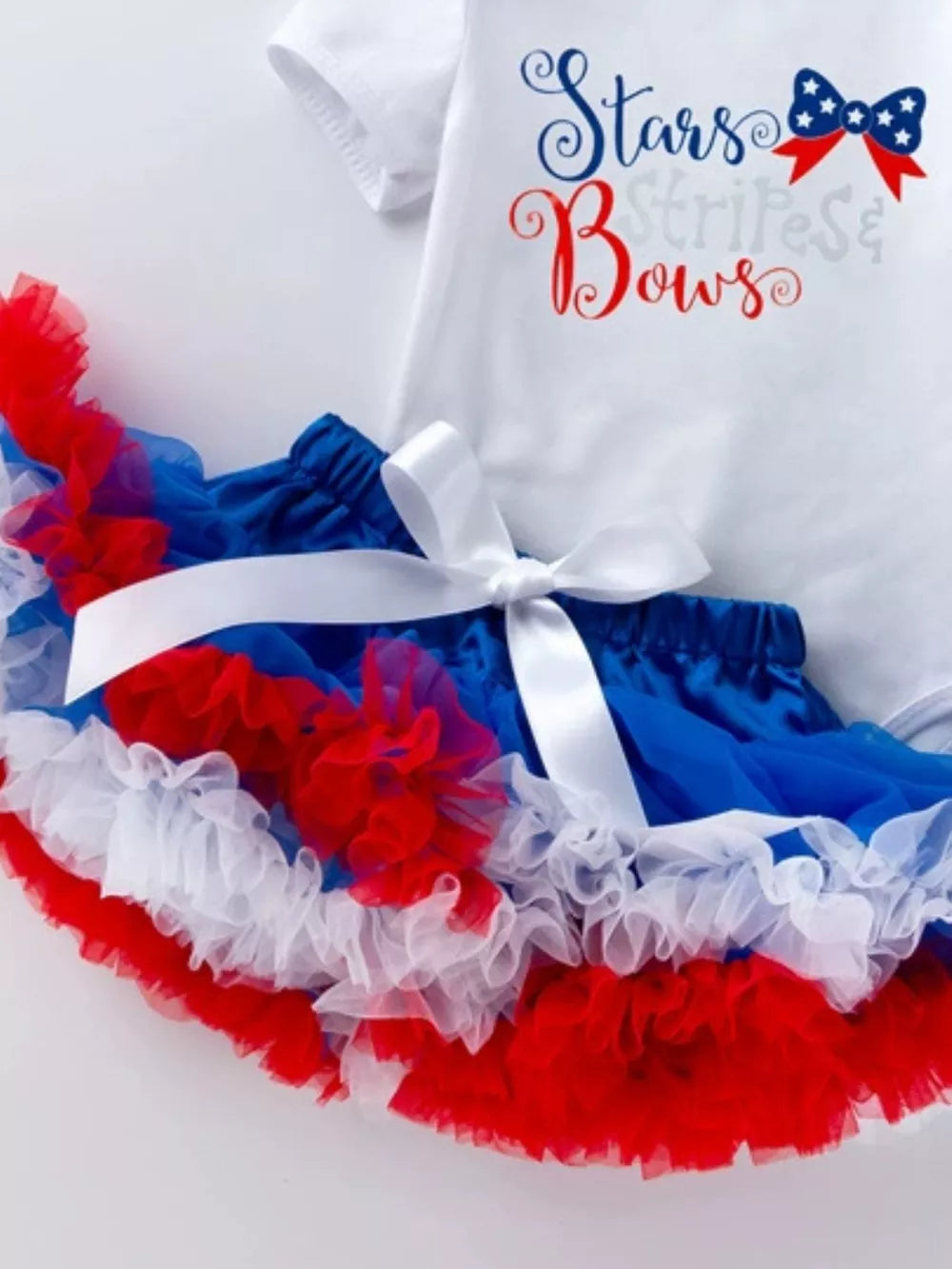 White baby onesie with "Stars Stripes & Bows" text and ruffled patriotic tutu with white ribbon.