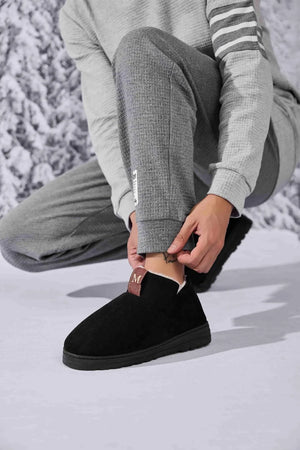 Black suede shearling-lined house booties with a brown logo tab.