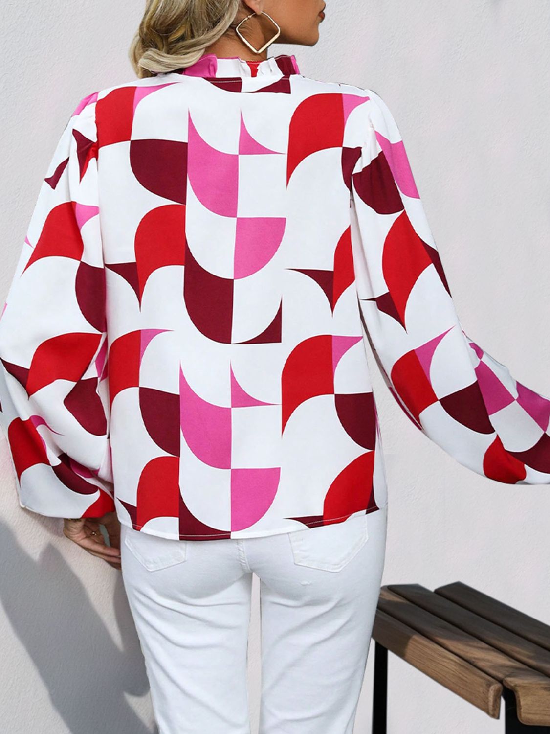 Geometric print blouse with voluminous sleeves and ruffled neckline in white with red and pink pattern.