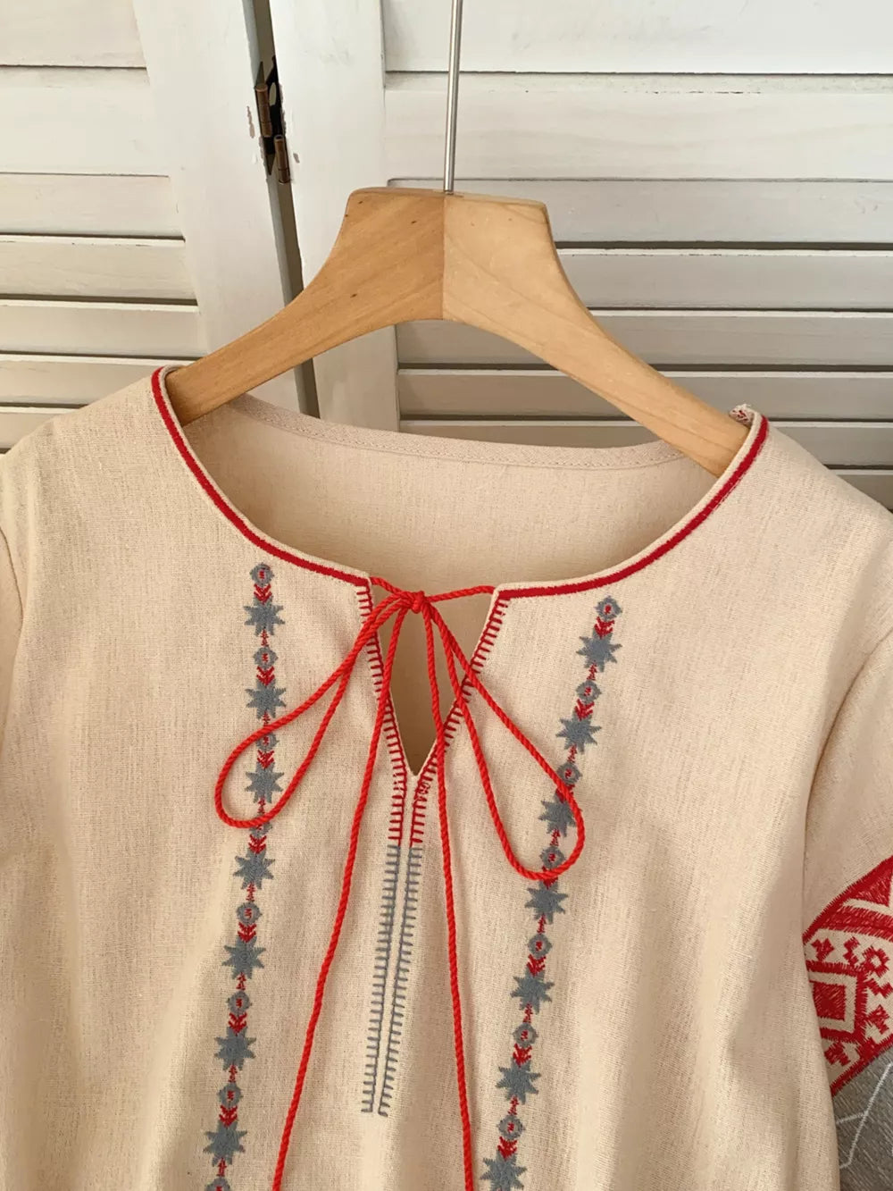 Apricot embroidered tie neck shirt with folk-inspired details and red trim.