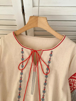 Apricot embroidered tie neck shirt with folk-inspired details and red trim.