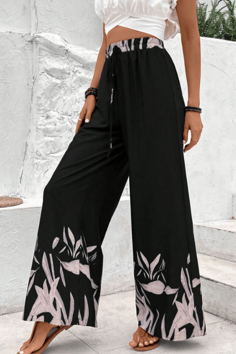 Black wide-leg lounge trousers with botanical print hem and drawstring waist.