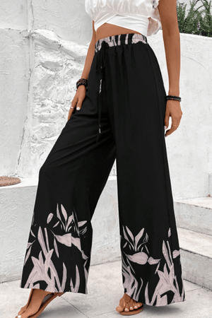 Black wide-leg lounge trousers with botanical print hem and drawstring waist.
