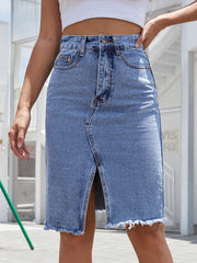 Slit-front frayed denim pencil skirt in medium blue with button closure and raw hem.
