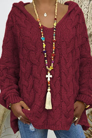 Burgundy cable knit hooded cocoon sweater with V-neck and tassel necklace.