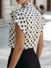 White and black polka dot polyester shirt with bow tie neck and cap sleeves.