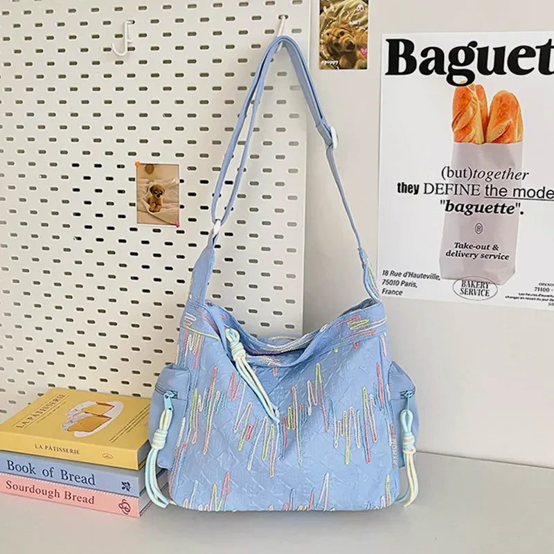 Light blue slouchy shoulder bag with colorful embroidered vertical lines and rope details.