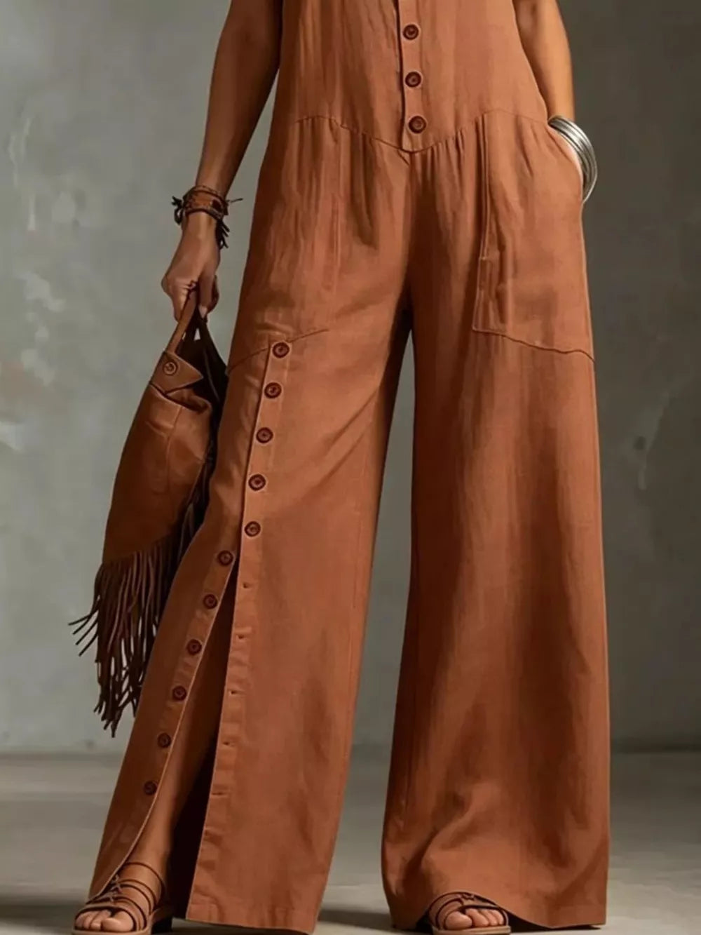 Caramel wide-leg jumpsuit with button details and pockets, styled with sandals and a fringe bag.