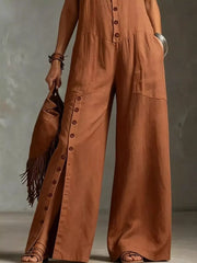 Caramel wide-leg jumpsuit with button details and pockets, styled with sandals and a fringe bag.