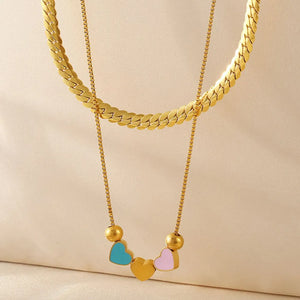 Gold double layered necklace with a flat herringbone chain and a delicate box chain featuring colorful heart charms.