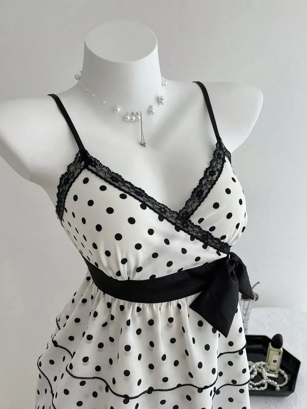 White polka dot camisole with black lace trim, black ribbon tie, and ruffled hem.