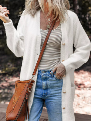 White fuzzy button-front cardigan with pockets and gold buttons, worn over a striped tank top.