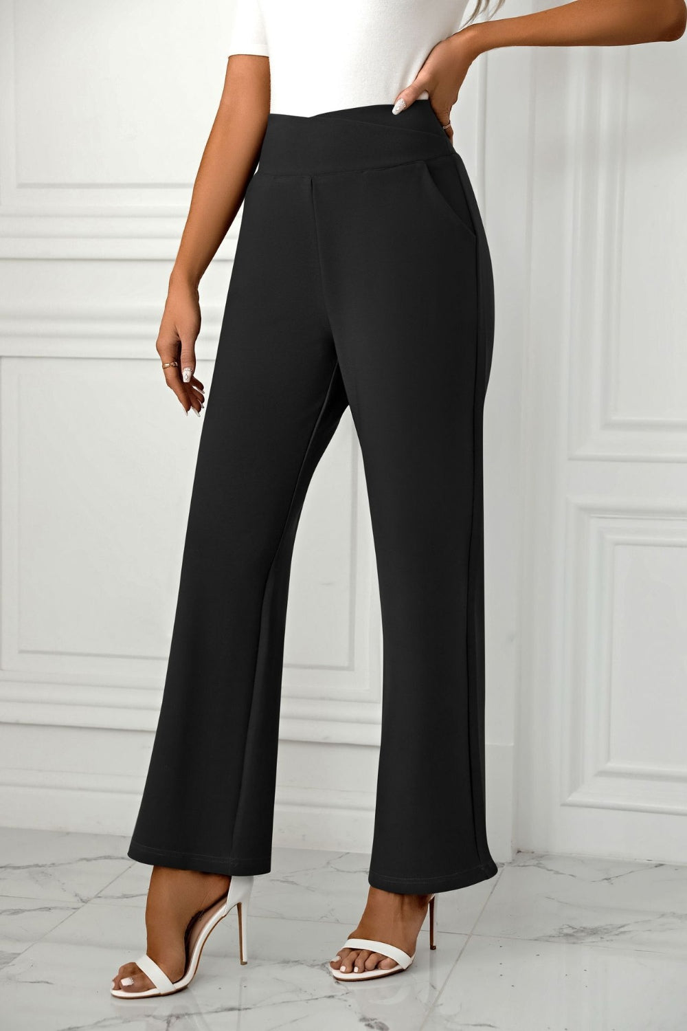 Black wide-leg trousers with sculpted waist and pockets, styled with white heels.