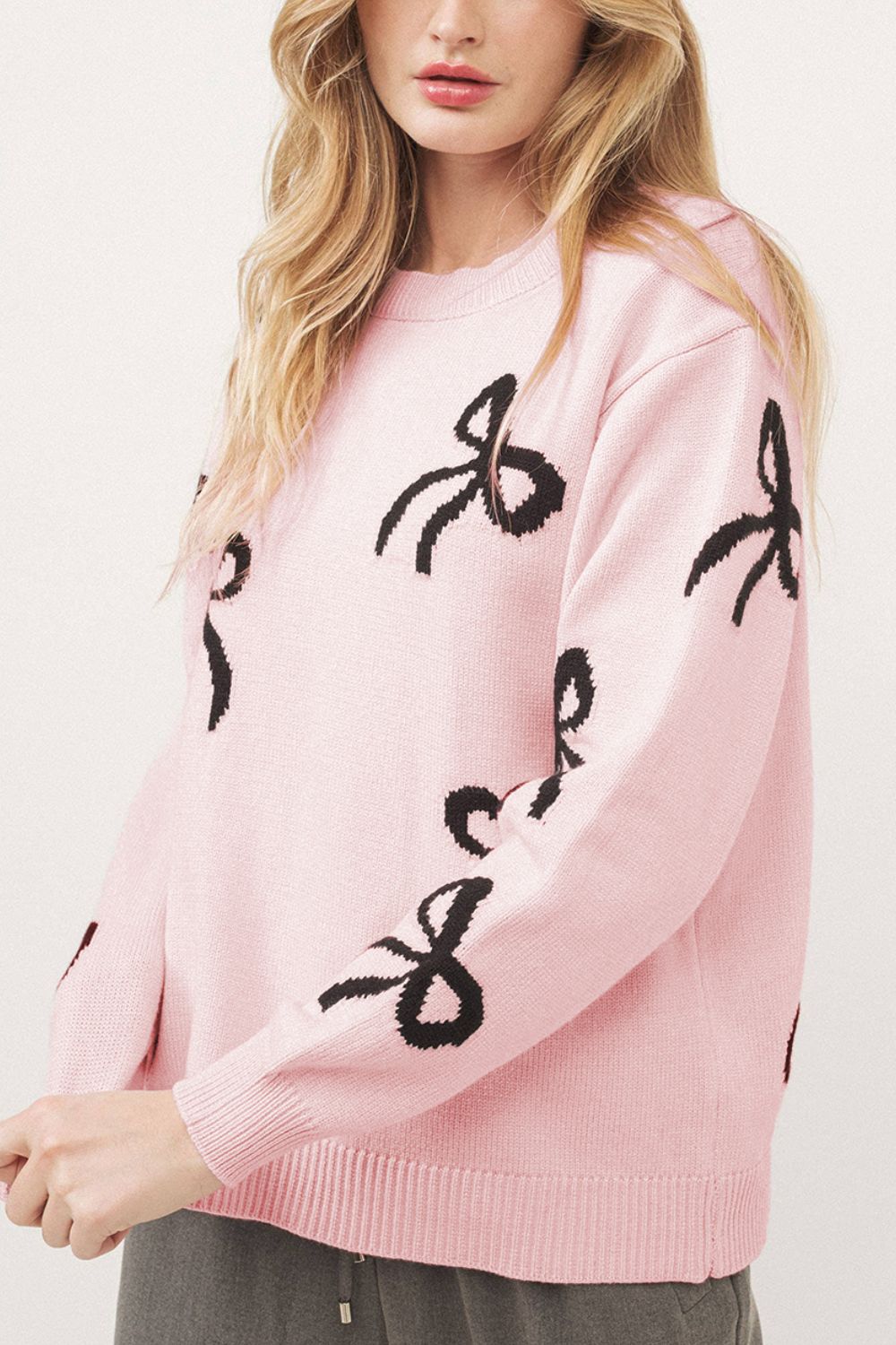 Blush pink knit crewneck sweater with allover black bow motifs.