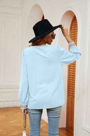 Light blue blouson top with embroidered trim on cuffs and V-neck.
