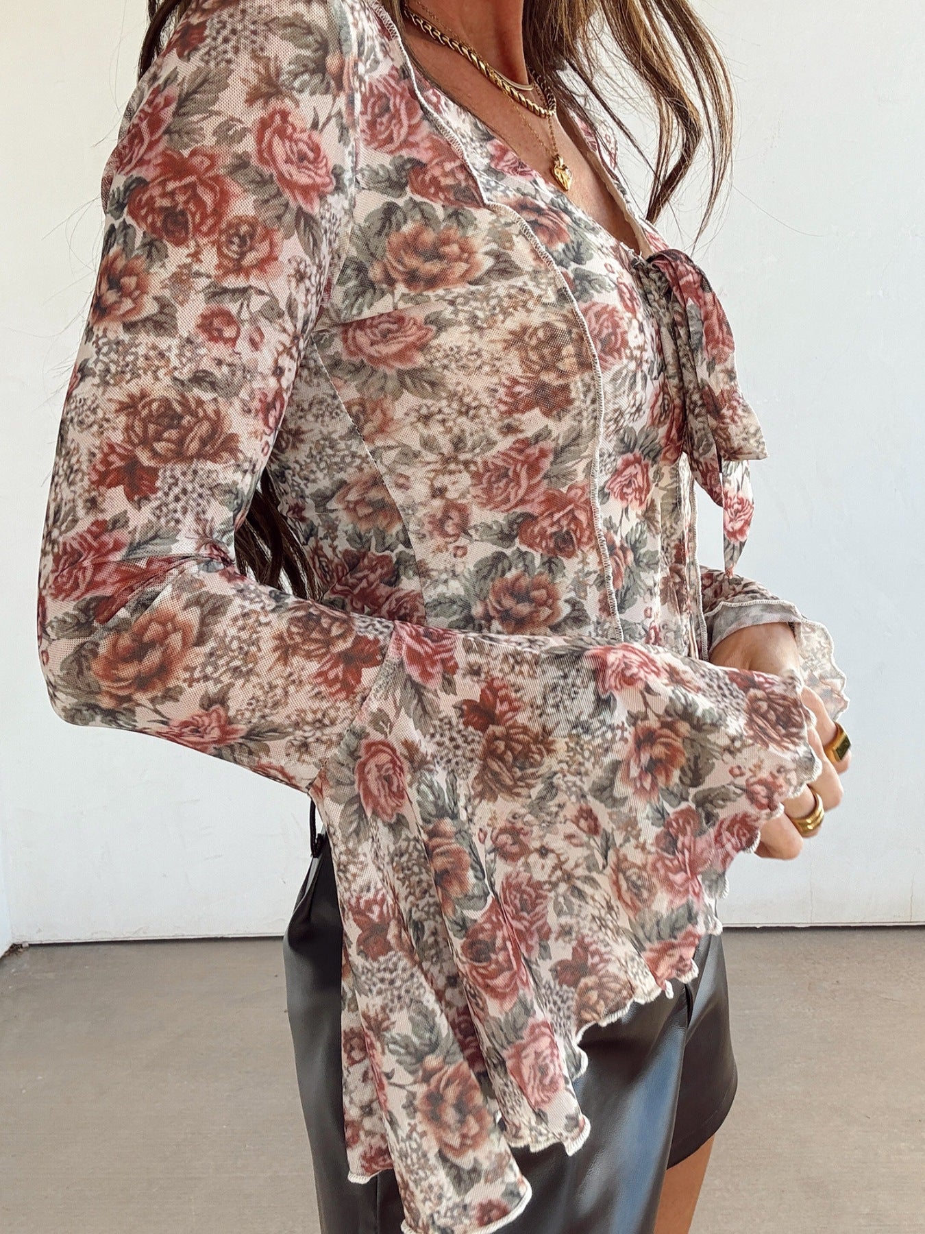 Charming floral mesh blouse with tied ruffle neckline and bell sleeves.