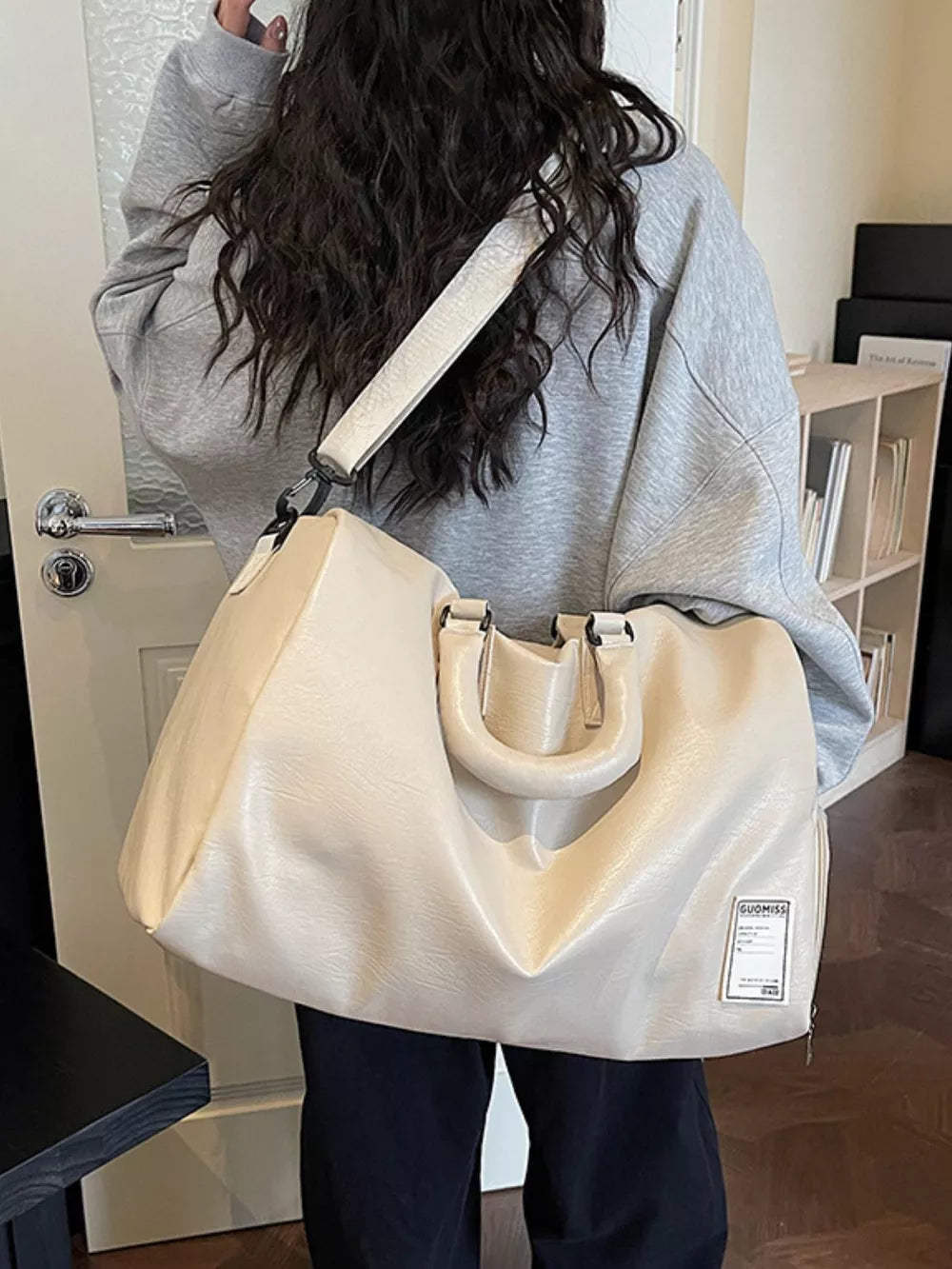 Spacious off-white pu leather travel duffel bag with top handles and shoulder strap.
