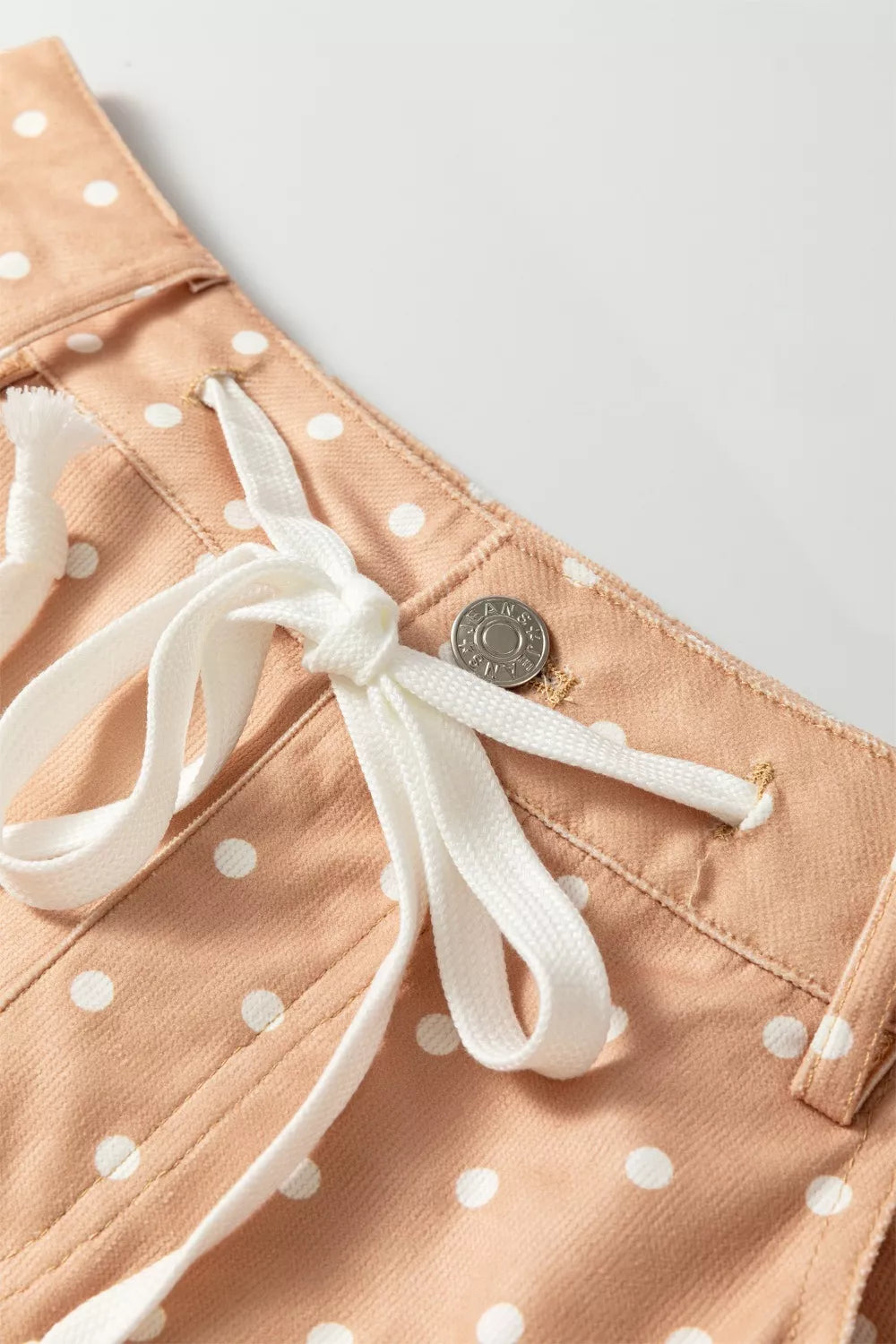 Peach polka dot maternity trousers with white drawstring and button detail.