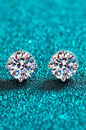Moissanite solitaire stud earrings with rhodium finish on a teal textured background.