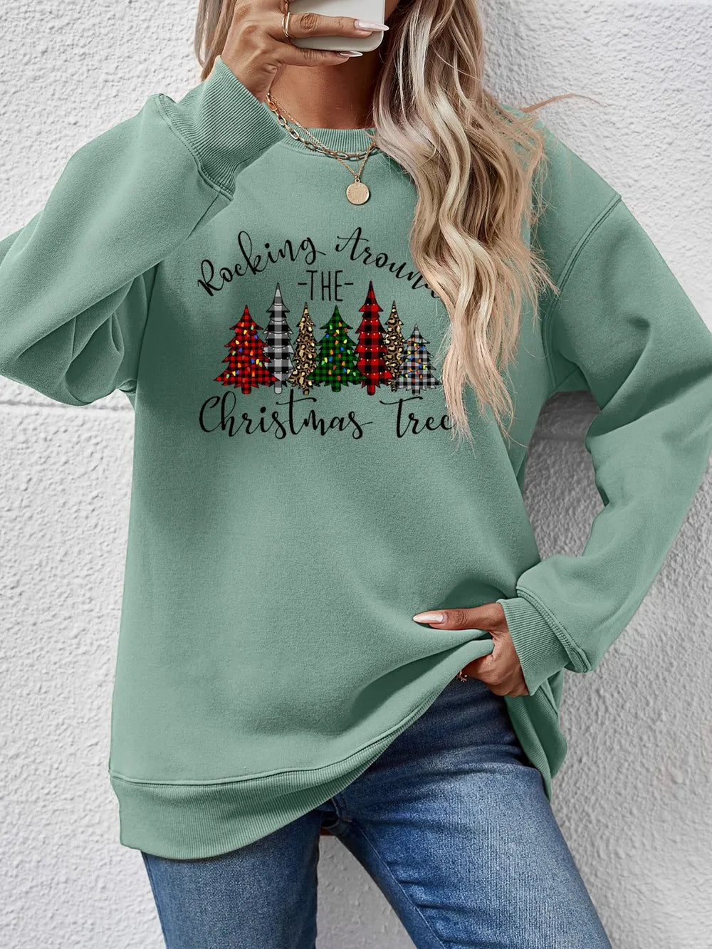 Sage green crewneck sweatshirt with a graphic of Christmas trees and "Rocking Around the Christmas Tree" text.