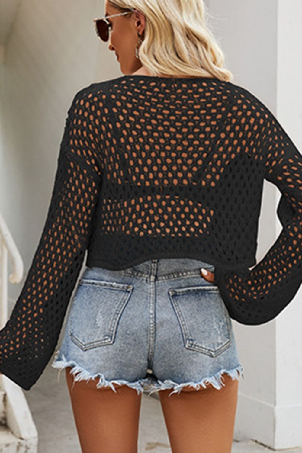 Black cropped open knit top with bell sleeves and a relaxed fit, styled with denim shorts.