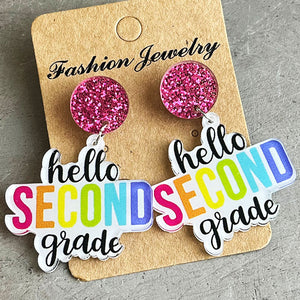 Acrylic drop earrings with pink glitter studs and "hello SECOND grade" text in rainbow colors.