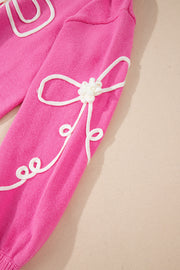 Fuchsia pink knit sweater with white embroidered bow motif detail on sleeve.