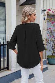 Black V-neck flutter sleeve blouse with back pleat detail and curved hem.