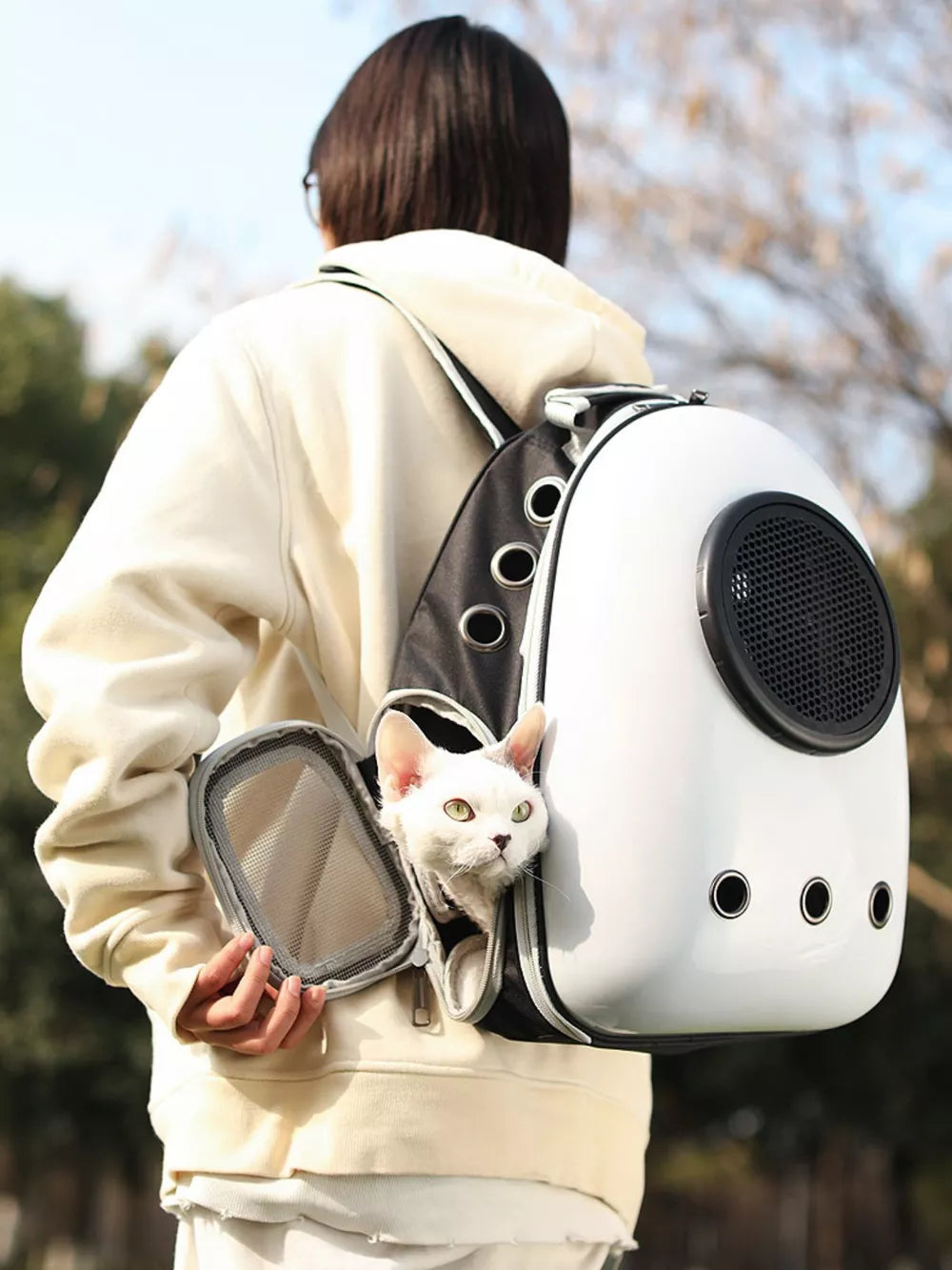 White and black pet carrier backpack with bubble window, a white cat peeking out.