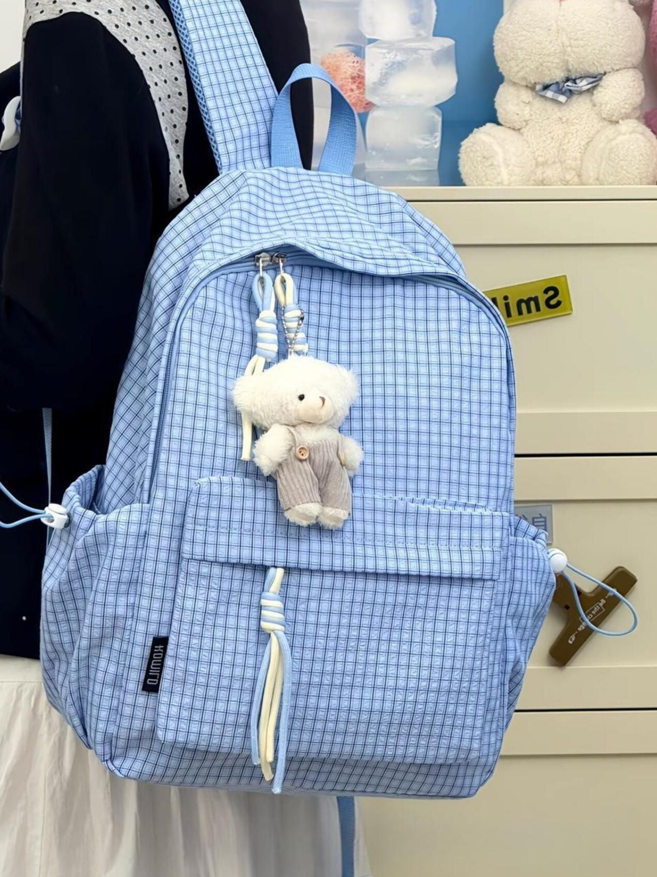 Blue plaid nylon backpack with teddy bear charm and tassel detail.
