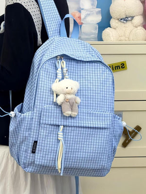 Blue plaid nylon backpack with teddy bear charm and tassel detail.