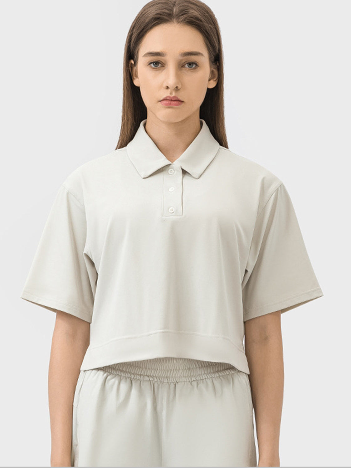 Cropped beige polo shirt with short sleeves and a button placket.