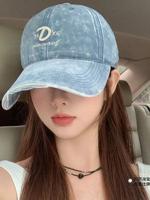 Blue denim baseball cap with embroidered D and text detail, distressed brim.