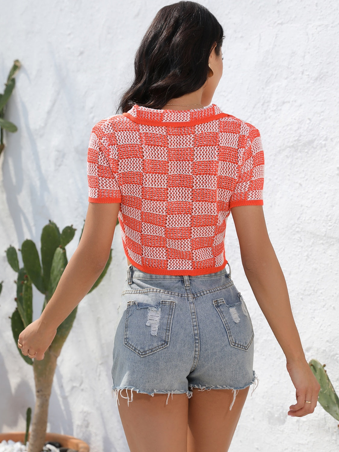 Orange-red and white checkerboard knit cropped polo shirt with short sleeves and collar.