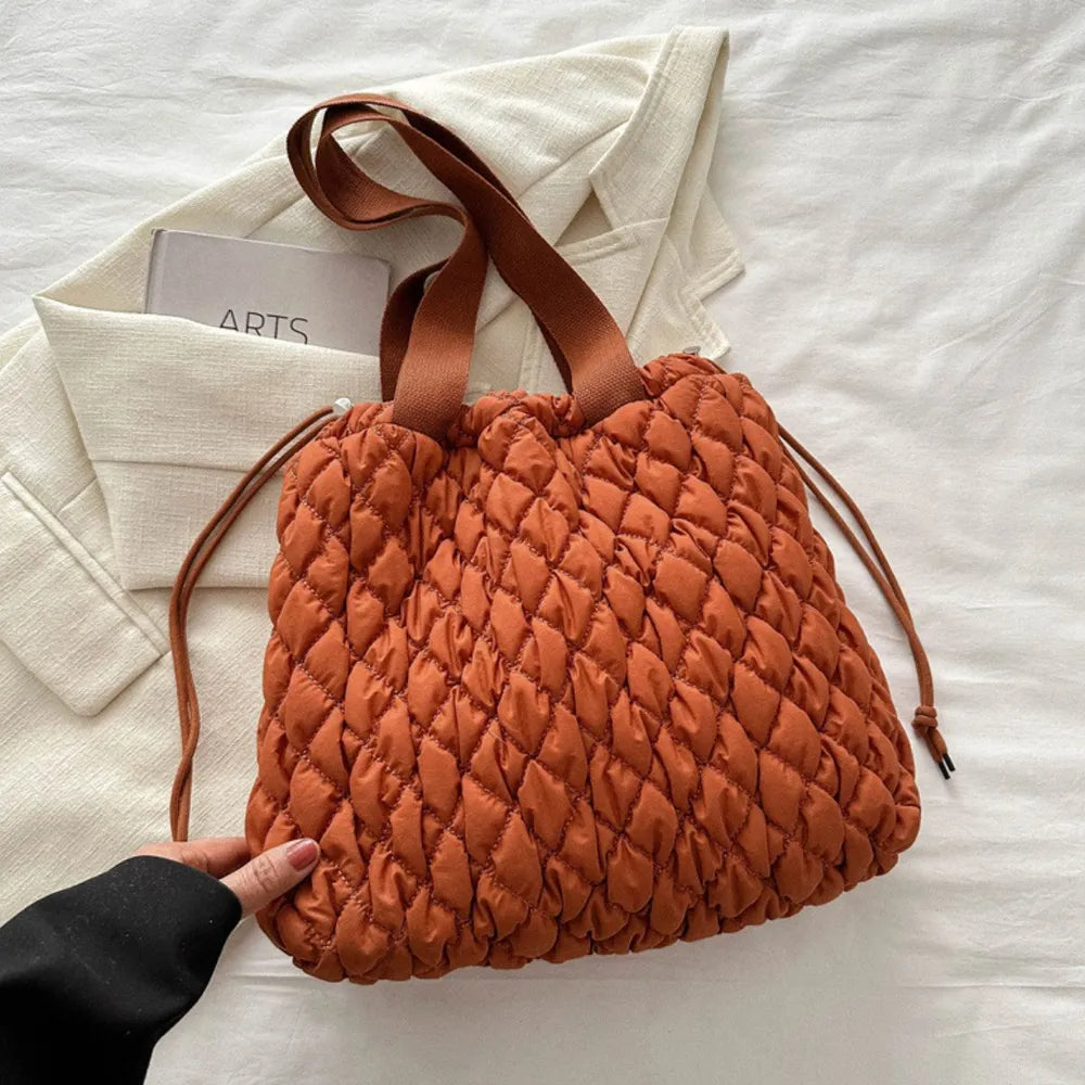 Terracotta quilted drawstring carryall bag with brown straps and cinched top.