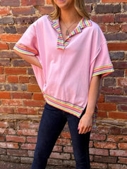 Pink cotton V-neck top with rainbow striped collar and cuffs, relaxed fit, exposed seams.