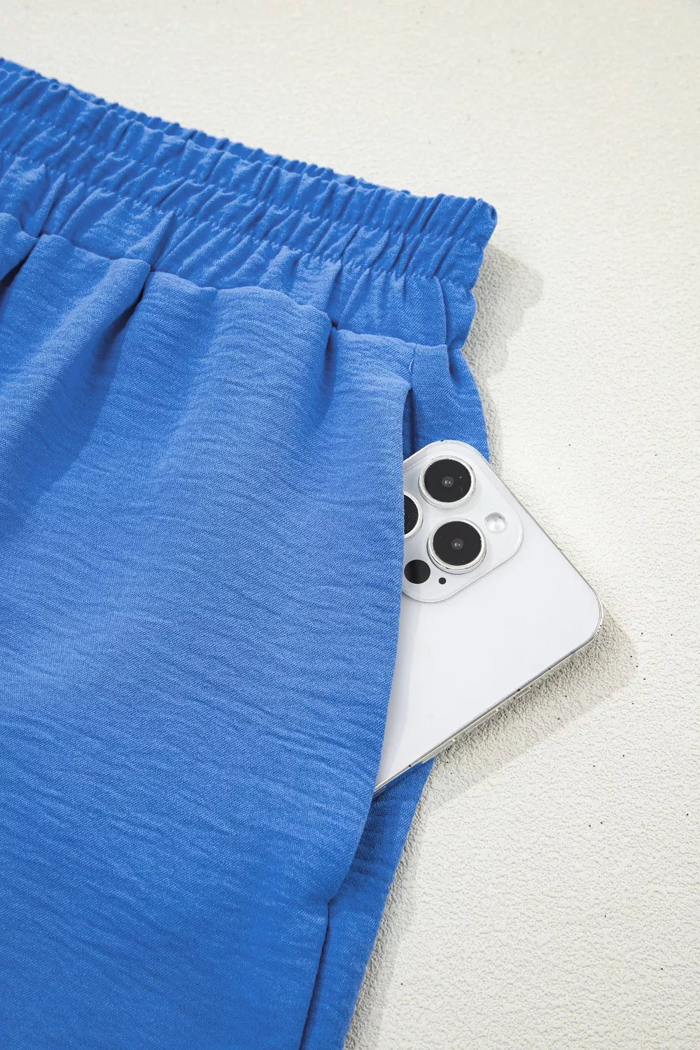 Blue textured drawstring shorts with elastic waistband and side pocket holding a phone.