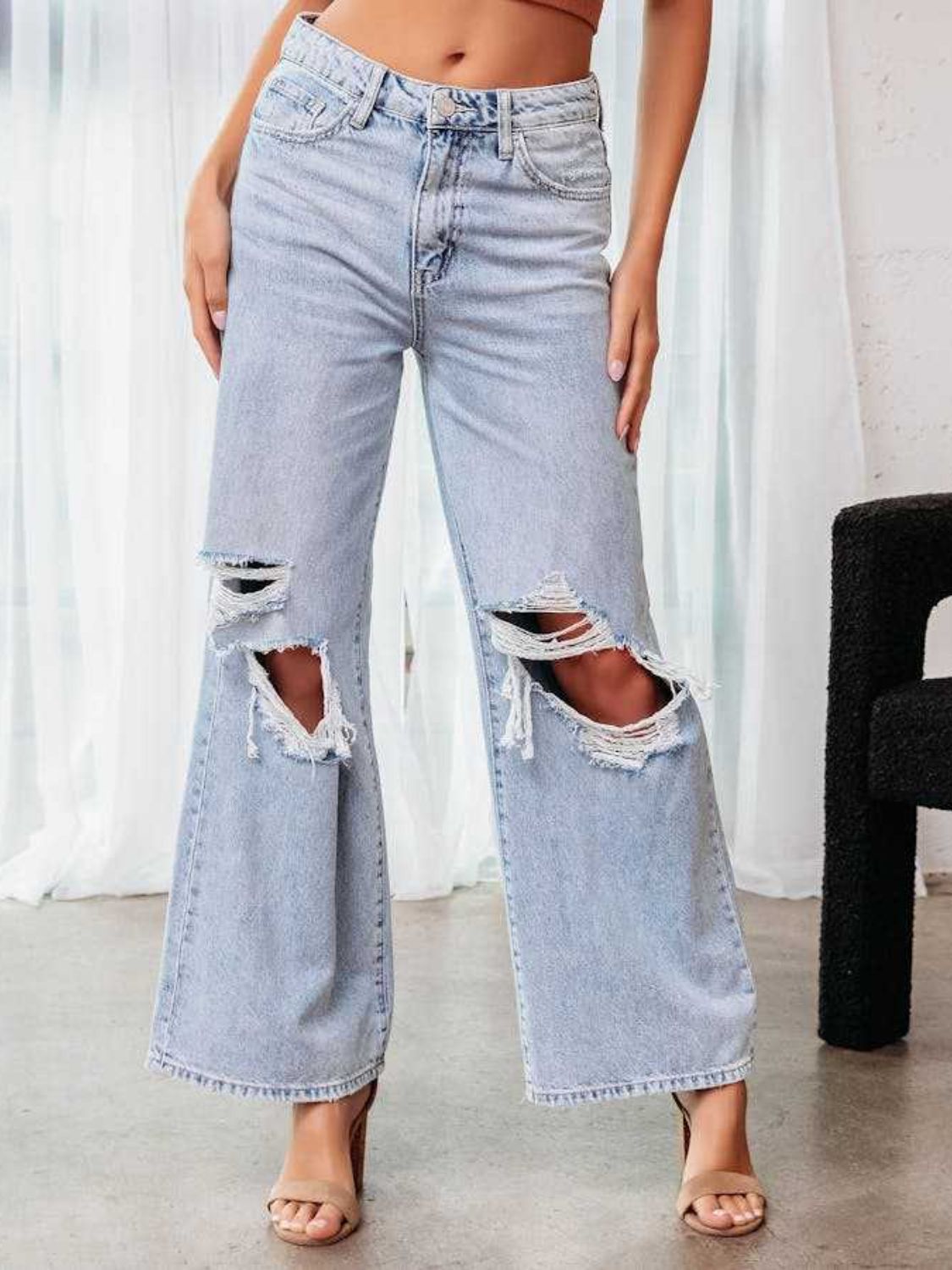 Distressed light wash denim wide leg flare jeans with ripped knees.