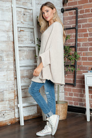 Relaxed knit sweater in cream with cape sleeves and a v-neck, styled with distressed jeans.