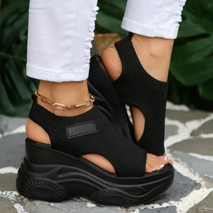 Black open-toe wedge sandals with chunky sole and ankle chain detail.